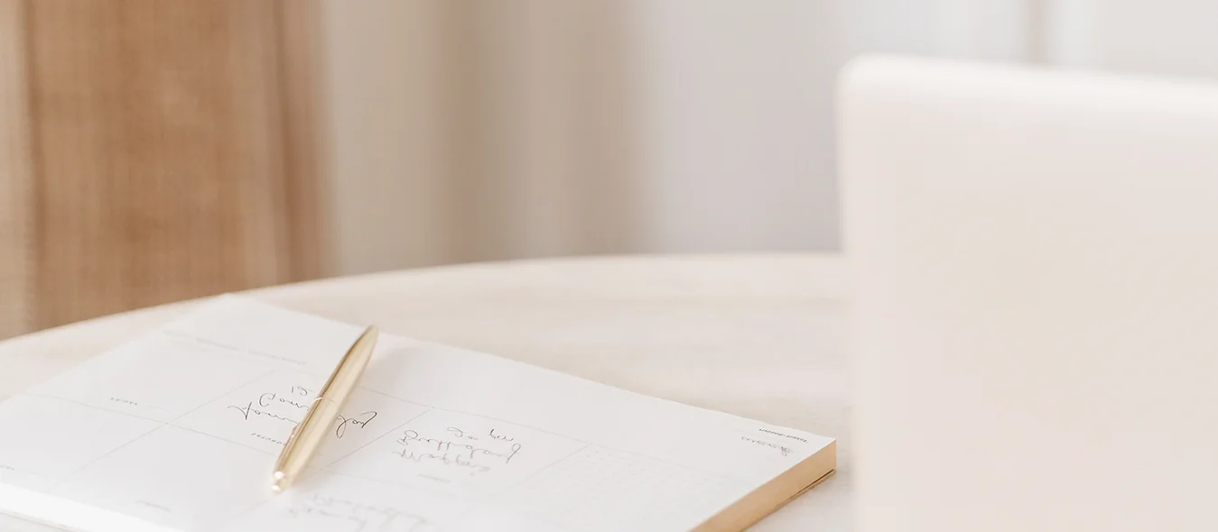 A notebook and pen on a table next to a laptop.