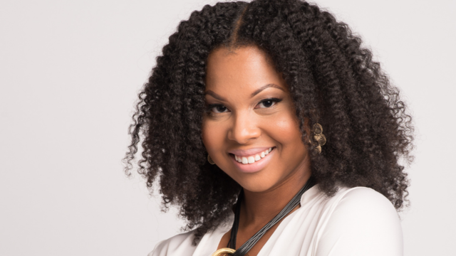 A black woman with a curly hair smiles in front of a white background.